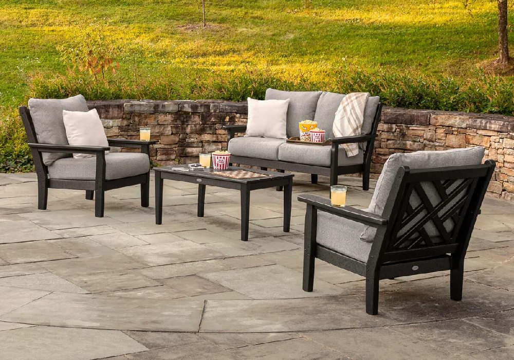 Commercial outdoor lounge furniture featuring cushioned club chairs and a sofa arranged around a coffee table on a stone patio.